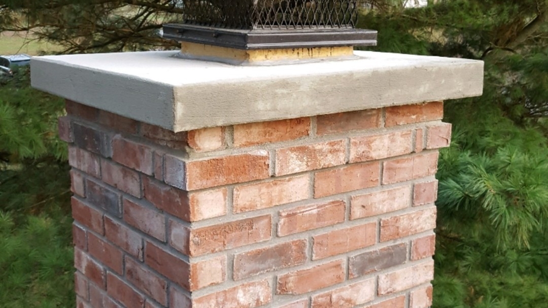 A newly capped brick chimney with a stainless steel spark-arrestor cap, repaired by Anything Masonry